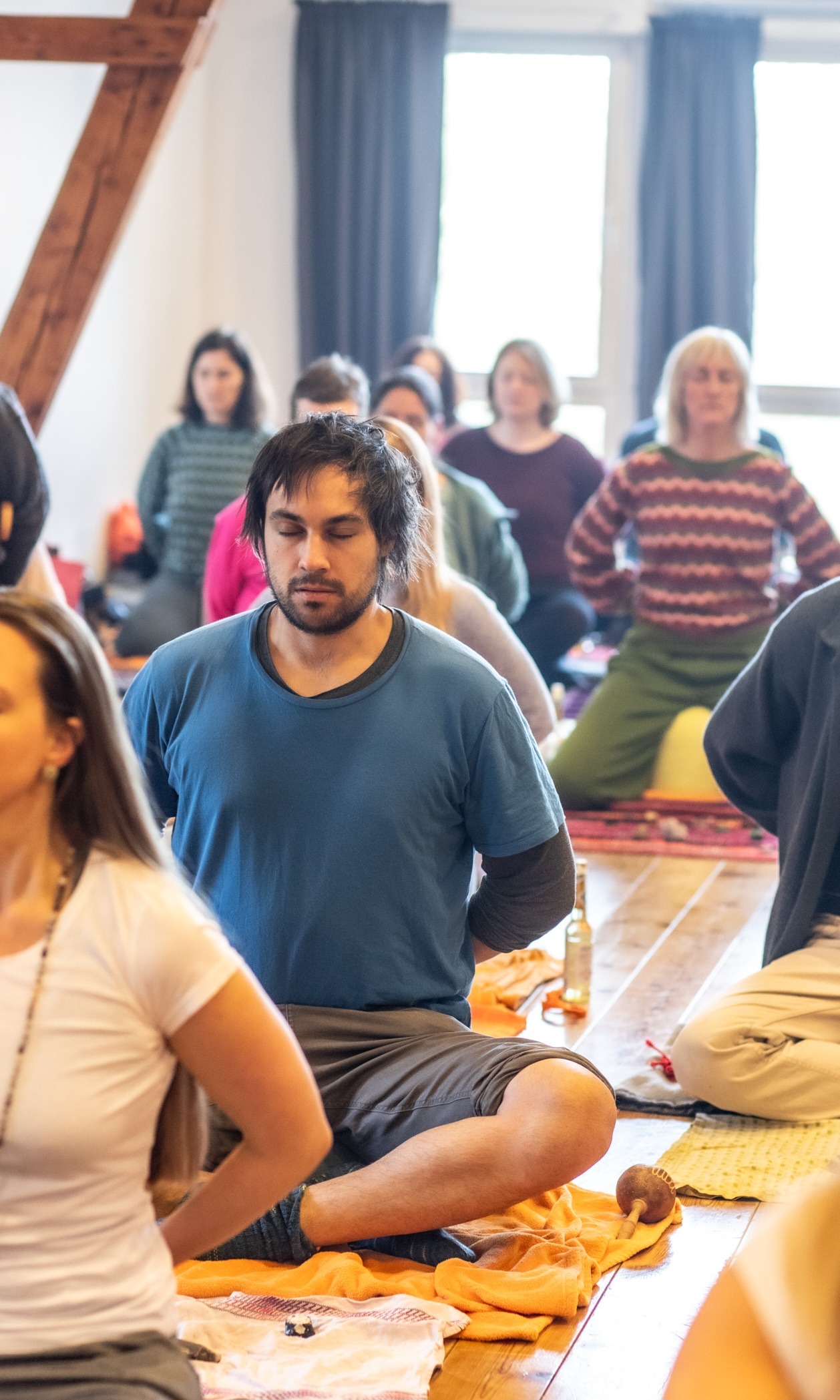 Hier sieht man im Rahmen der Ausbildung zum Shamanic Practitioner im Vordergrund des Bildes einen jungen Mann in Meditation; um ihn herum verschwommen weitere Personen in Meditation.