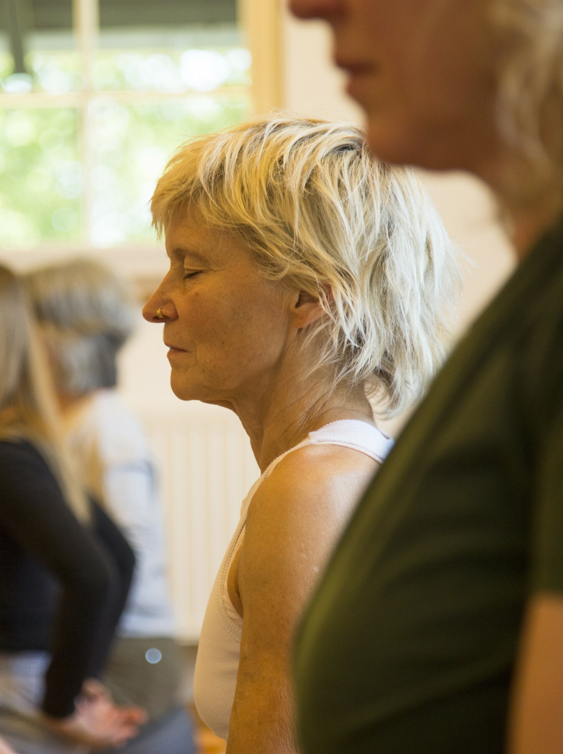 Man sieht eine Frau Anfang 50, hellblondes kurzes Haar, tief versunken in Meditation im Rahmen eines Stille-Retreats.