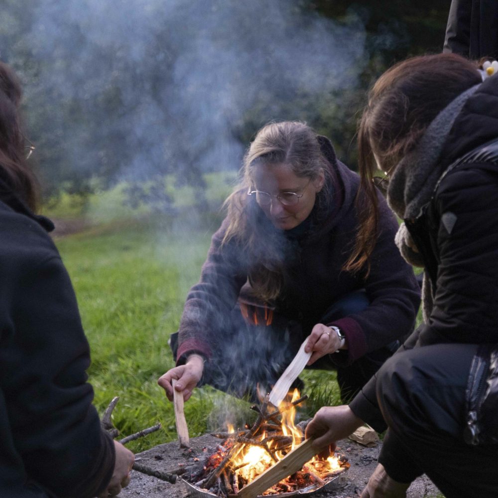 Man sieht im Rahmen des schamanischen Transformations-Retreats eine kleine Gruppe von Frauen in ihren Vierzigern, die ein Feuer entzünden.